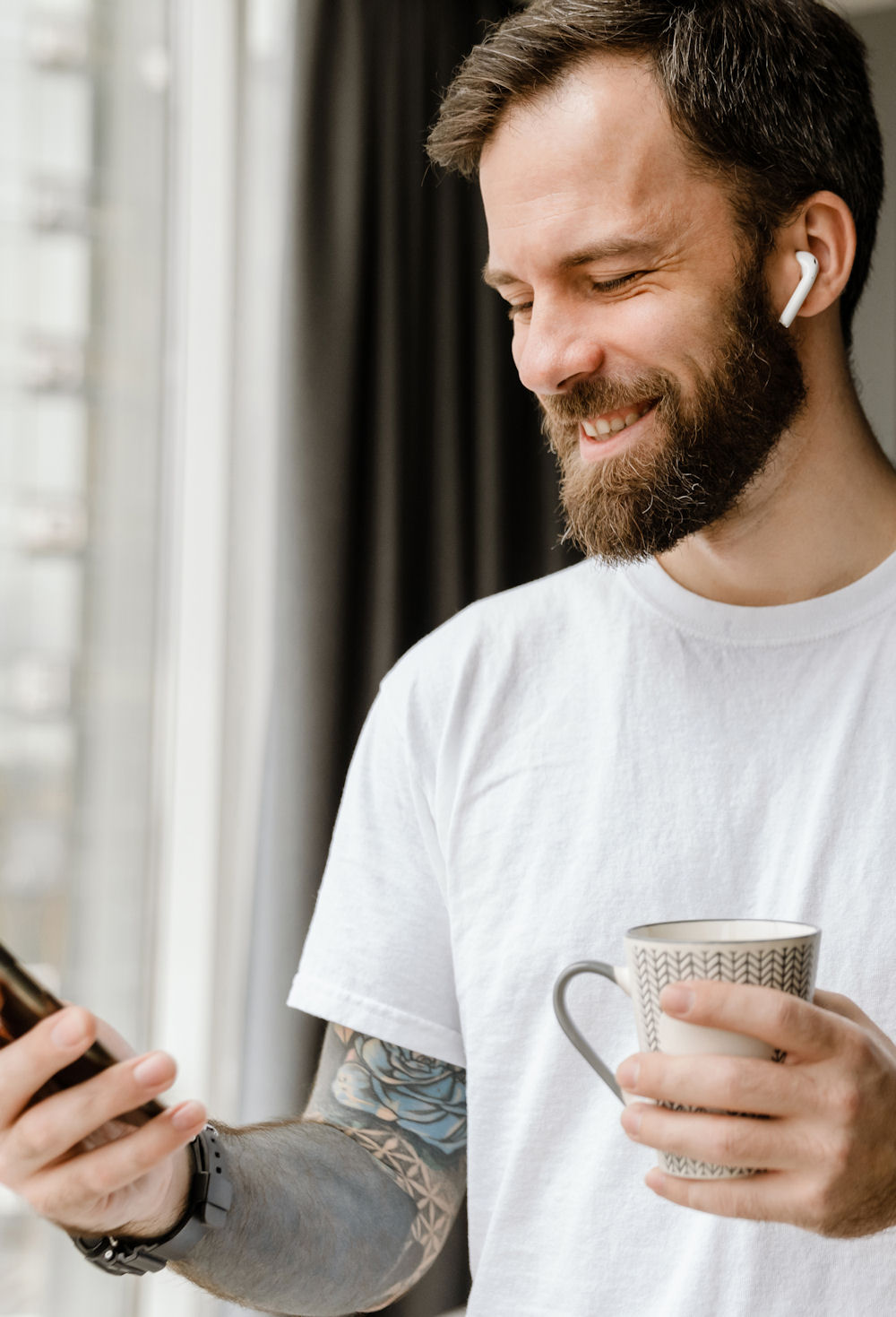 Bearded european man drinking coffee while using mobile phone at